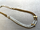 top view of gemstone bead necklace comprising white pearl, gold hematite and bronze dot accents.