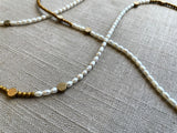 closeup view of gemstone bead necklace comprising white pearl, gold hematite and bronze dot accents.
