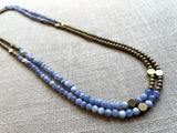 top view of gemstone bead necklace comprising periwinkle iolite, light gold hematite and bronze hex accents.