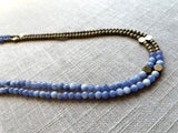 side view of gemstone bead necklace comprising periwinkle iolite, light gold hematite and bronze hex accents.