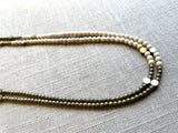 side view of gemstone bead necklace comprising off-white fossil jasper, light gold hematite and bronze hex accents.