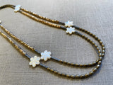top view of gemstone bead necklace comprising white carved shell flowers, cream shell, light gold hematite and grey pyrite.