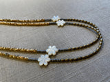 side view of gemstone bead necklace comprising white carved shell flowers, cream shell, light gold hematite and grey pyrite.