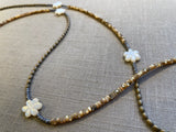 closeup view of gemstone bead necklace comprising white carved shell flowers, cream shell, light gold hematite and grey pyrite.