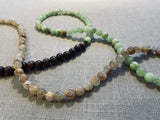 closeup view of gemstone bead necklace comprising green calcite, light yellow rutilated quartz and brown exotic wood.