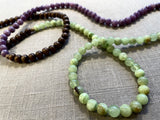 closeup view of gemstone bead necklace comprising purple lepidolite, green calcite and brown exotic wood.