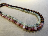 top view of gemstone bead necklace comprising pink strawberry quartz, green prehnite and brown exotic wood.