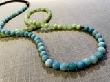closeup view of gemstone bead necklace comprising blue larimar, green calcite and brown exotic wood.