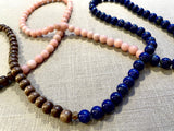 top view of gemstone bead necklace comprising pink opal, blue lapis and brown exotic wood.