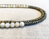 side view of gemstone bead necklace comprising white siberian moonstone, neutral shell and dark grey pyrite