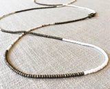 closeup of gemstone bead necklace comprising white shell and light gold hematite
