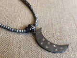 closeup of pave crescent moon pendant hung on metallic bead choker