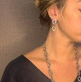 Close-up of a person wearing silver hoop earrings and a chain necklace against a neutral background