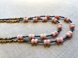 side view of gemstone bead necklace comprising pink opal, grey pyrite and bronze. 
