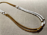 top view of gemstone bead necklace comprising white howlite, gold and silver hematite and bronze hex accents. 
