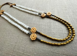 top view of gemstone bead necklace comprising antique hand-carved bone flowers, white rainbow moonstone and gold hematite