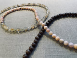 closeup view of gemstone bead necklace comprising pink opal, light yellow rutilated quartz and brown exotic wood. 