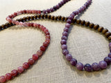 closeup view of gemstone bead necklace comprising purple lepidolite, pink strawberry quartz and brown exotic wood. 