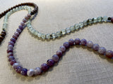 closeup view of gemstone bead necklace comprising purple lepidiolite, green prehnite and brown exotic wood. 