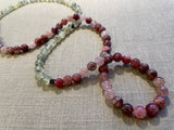 closeup view of gemstone bead necklace comprising pink strawberry quartz, green prehnite and brown exotic wood. 