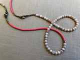 top view of gemstone bead necklace comprising pink opal, pink vinyl disk and bronze mariners links.