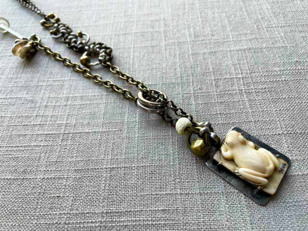 closeup of antique carved fossilized ivory frog pendant on chain mix