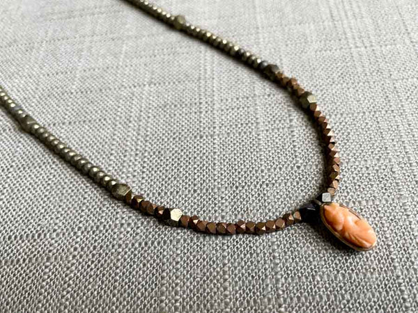 closeup of antique coral cameo pendant hung on a metallic bead choker