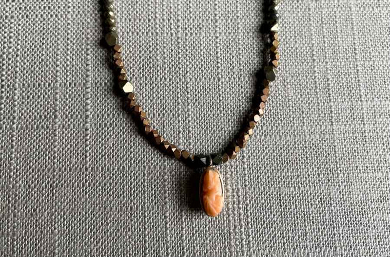 closeup of antique coral cameo pendant hung on a metallic bead choker
